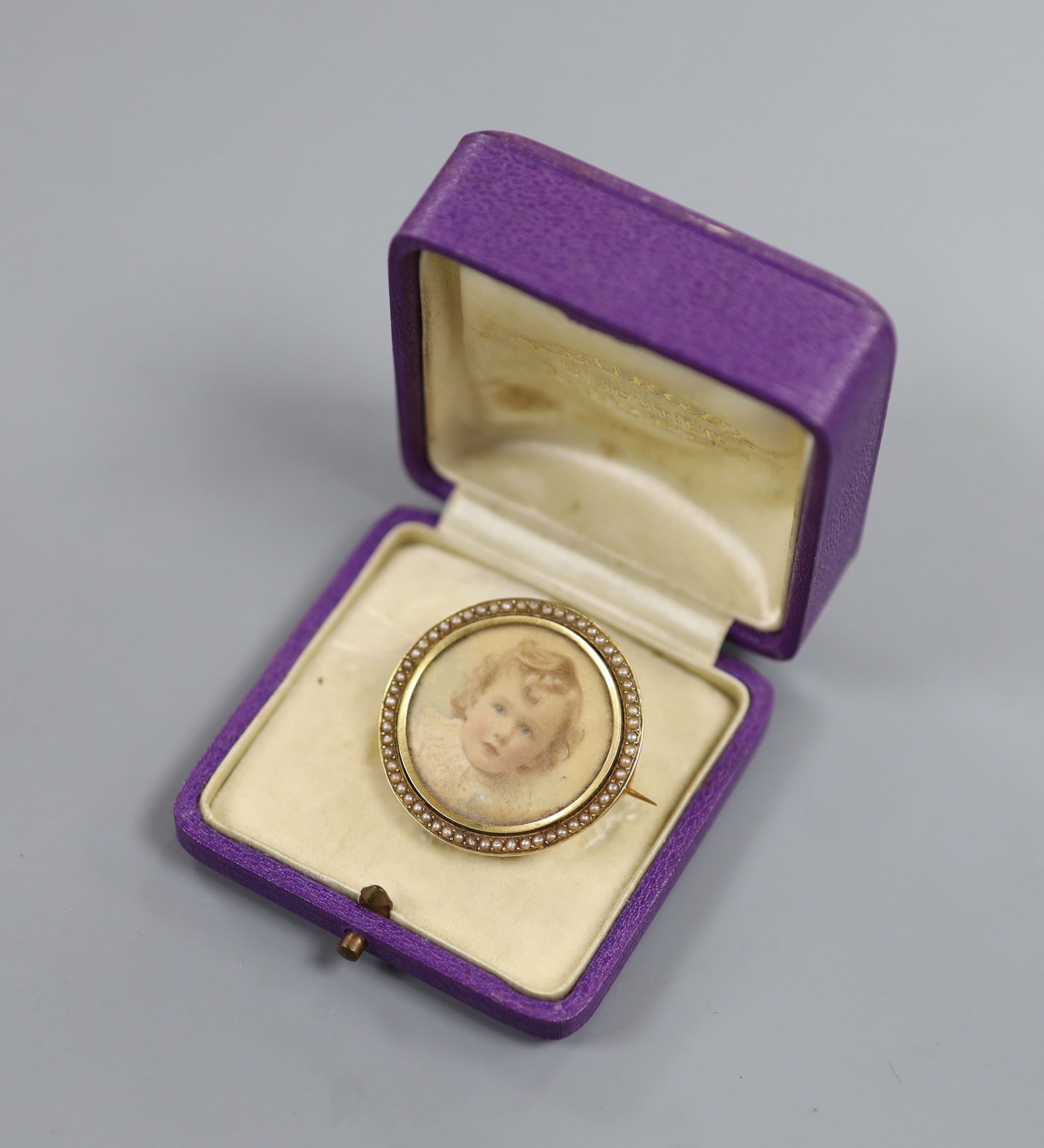 An early 20th century yellow metal and split pearl set circular brooch, inset with portrait of a young, verso with hair beneath a glazed panel, 34mm, gross weight 11.4 grams.